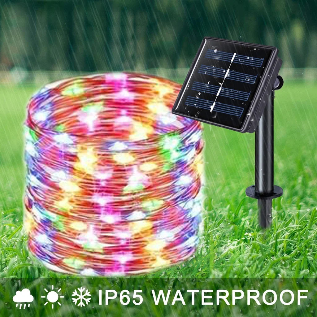 A coil of colorful fairy string lights is shown next to a solar-powered outdoor light fixture on green grass.