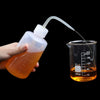 A hand is squeezing an orange liquid from a plastic bottle into a glass measuring cup using a precision tip.