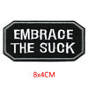 Black embroidered iron-on letter patch with white text that reads Embrace the Suck