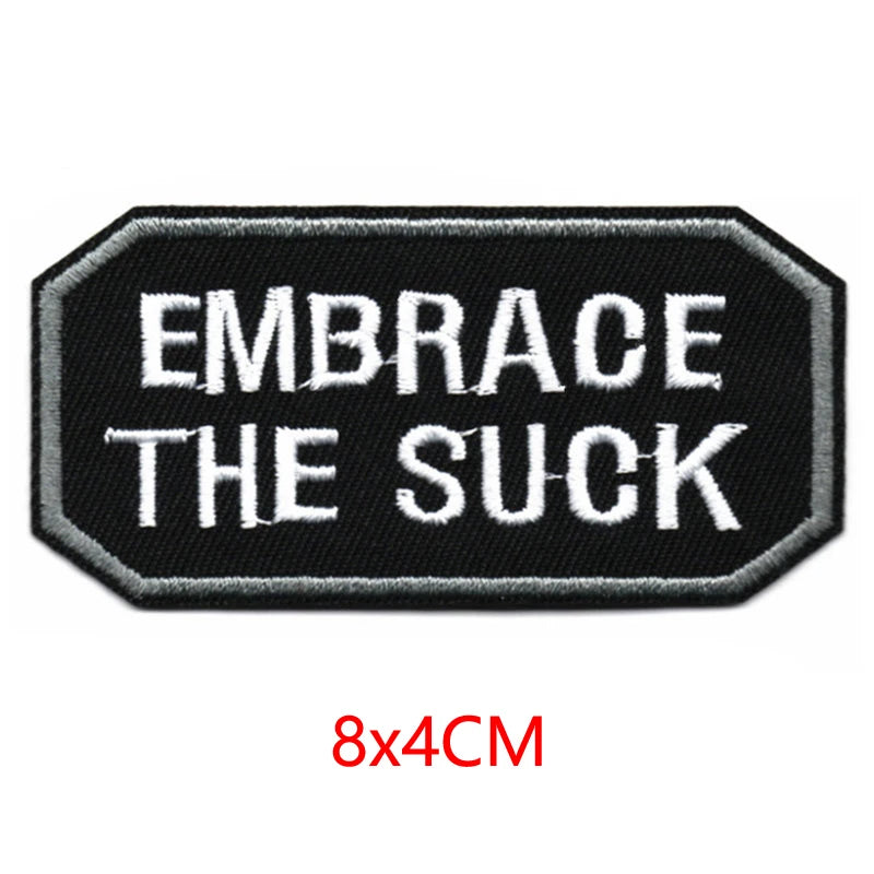 Black embroidered iron-on letter patch with white text that reads Embrace the Suck