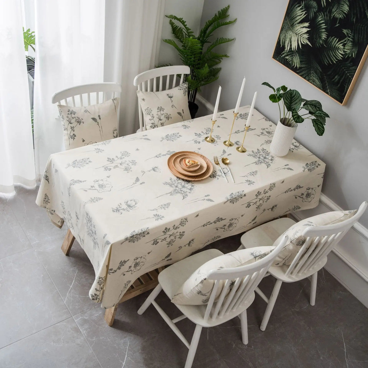 A dining table set with a cream tablecloth featuring a rustic fern print, surrounded by white wooden chairs.
