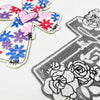 Embroidered patch featuring a cross design with pink, blue, and red floral elements on white fabric.