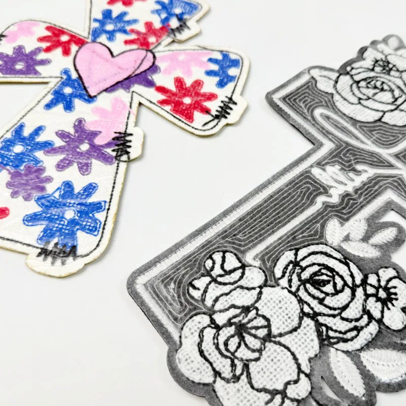 Embroidered patch featuring a cross design with pink, blue, and red floral elements on white fabric.