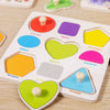 A wooden 3D jigsaw puzzle board with various colored shapes like circles, squares, hearts, and pentagons for toddlers.
