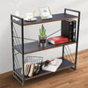 A black metal tiered shelf rack with three levels holding various items like a photo frame, potted plant, and books.