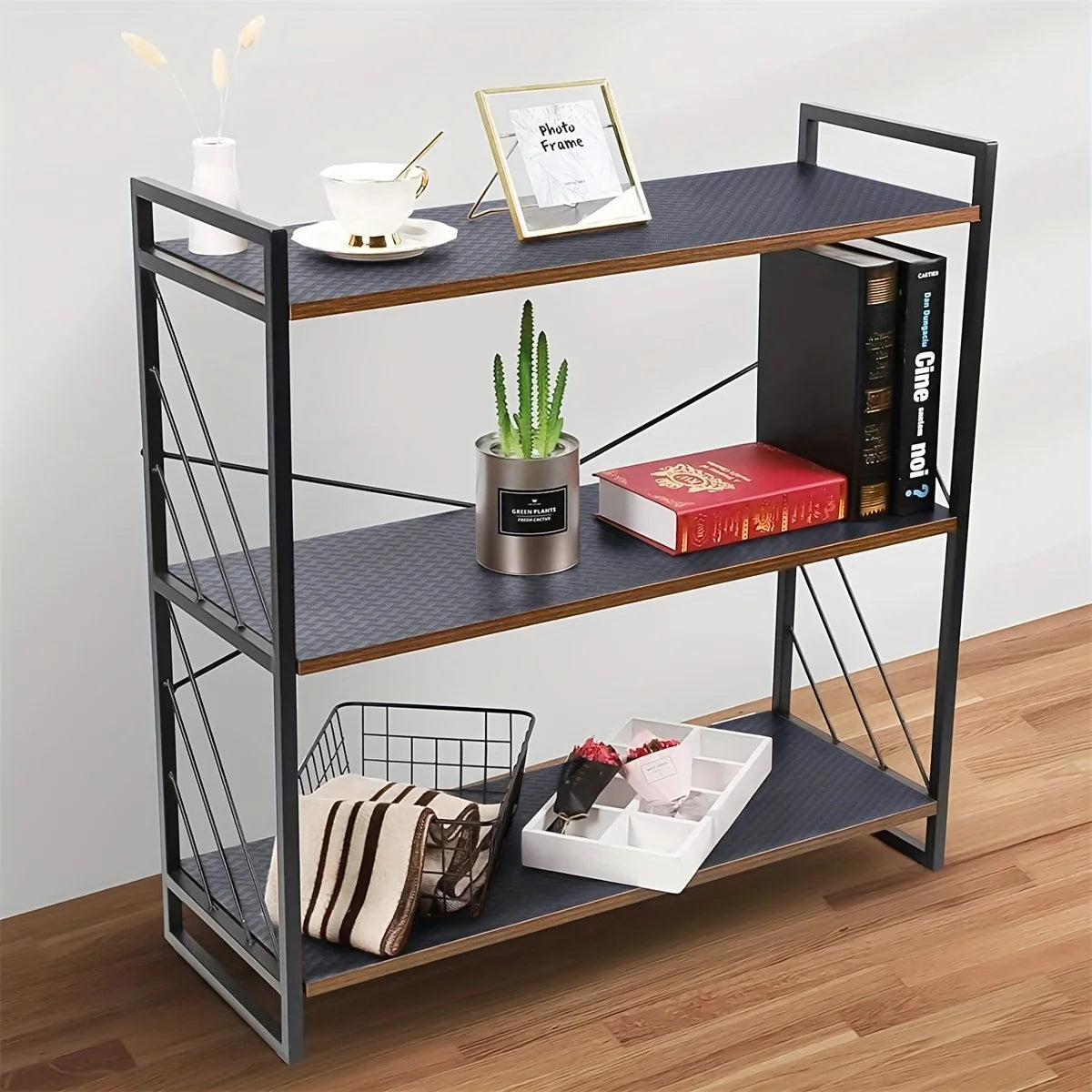 A black metal tiered shelf rack with three levels holding various items like a photo frame, potted plant, and books.