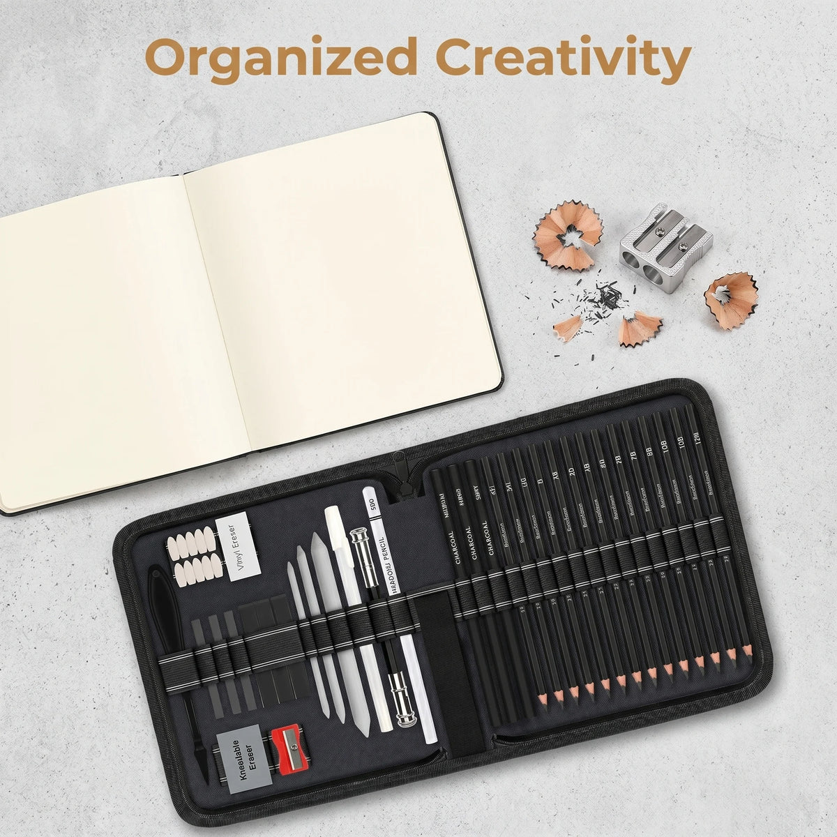 A black drawing sketch kit with graphite and charcoal pencils is displayed next to an open notebook.