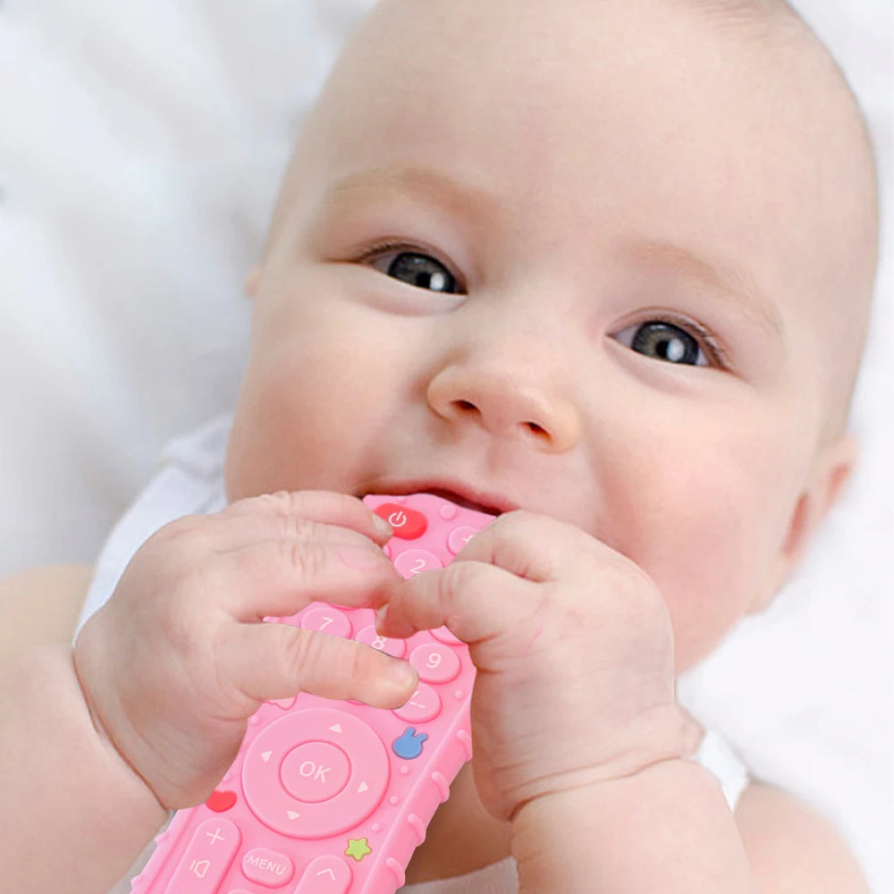 A baby is holding a pink silicone teether toy shaped like a TV remote.