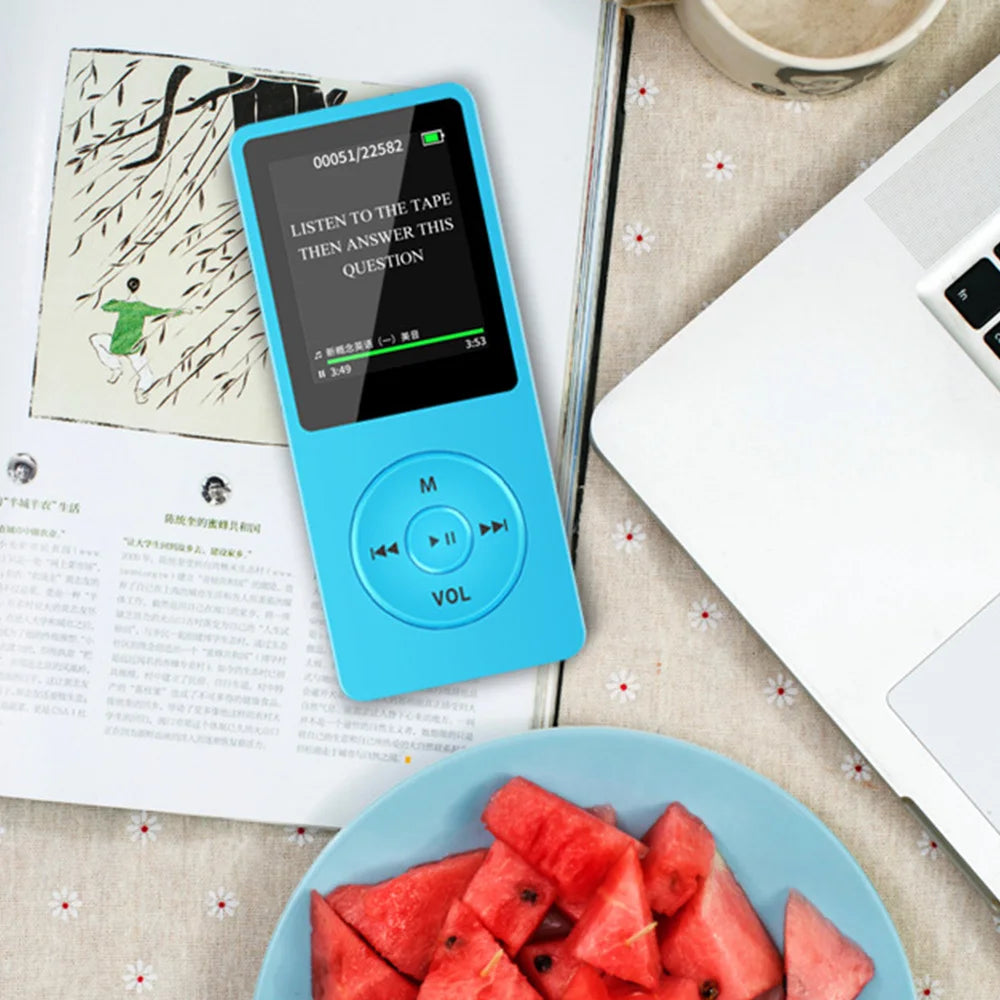 A blue compact MP3 player with an LCD screen is shown next to some papers and fruit.