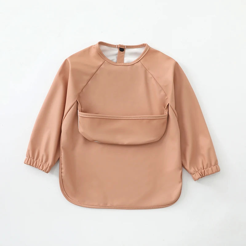 A light beige waterproof long-sleeve smock for toddlers with a rounded neckline and patch pockets.