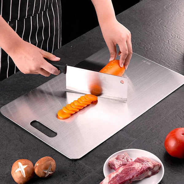 A stainless steel cutting board is shown with sliced carrots and raw meat on a dark surface.