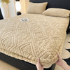 A beige plush mattress cover with an elastic edge is shown on a dark bed.