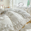 A white ruffled duvet cover set with pillows and a decorative stuffed animal on a bed.