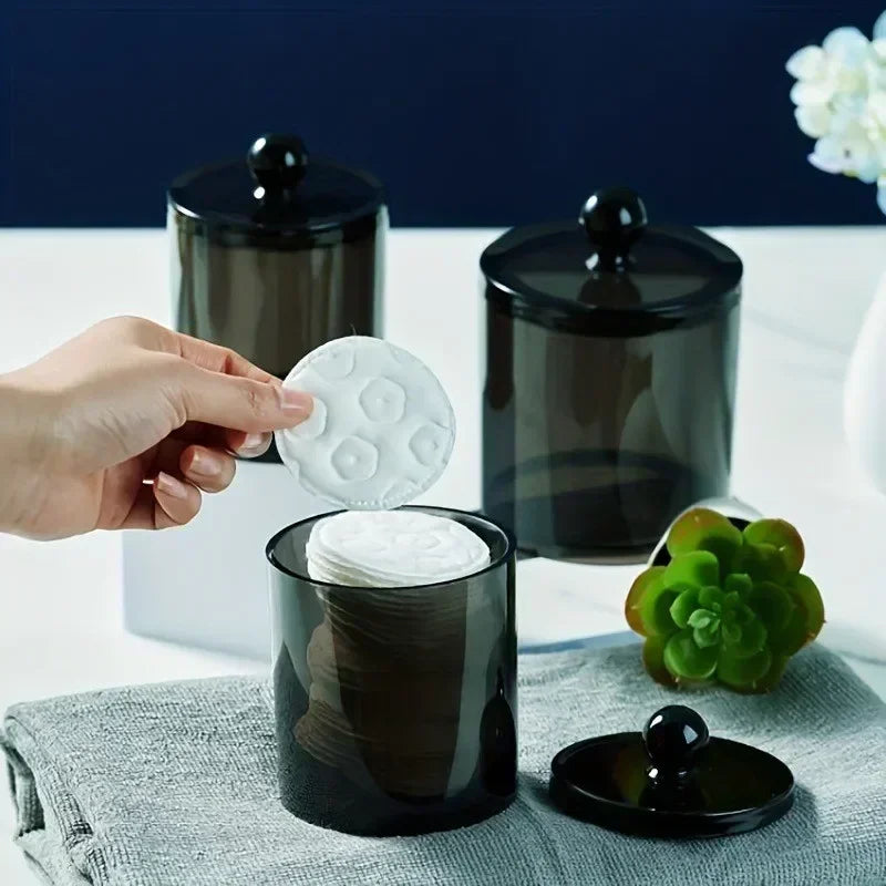 A set of clear apothecary jars with black lids and white round lids for storage and organization.