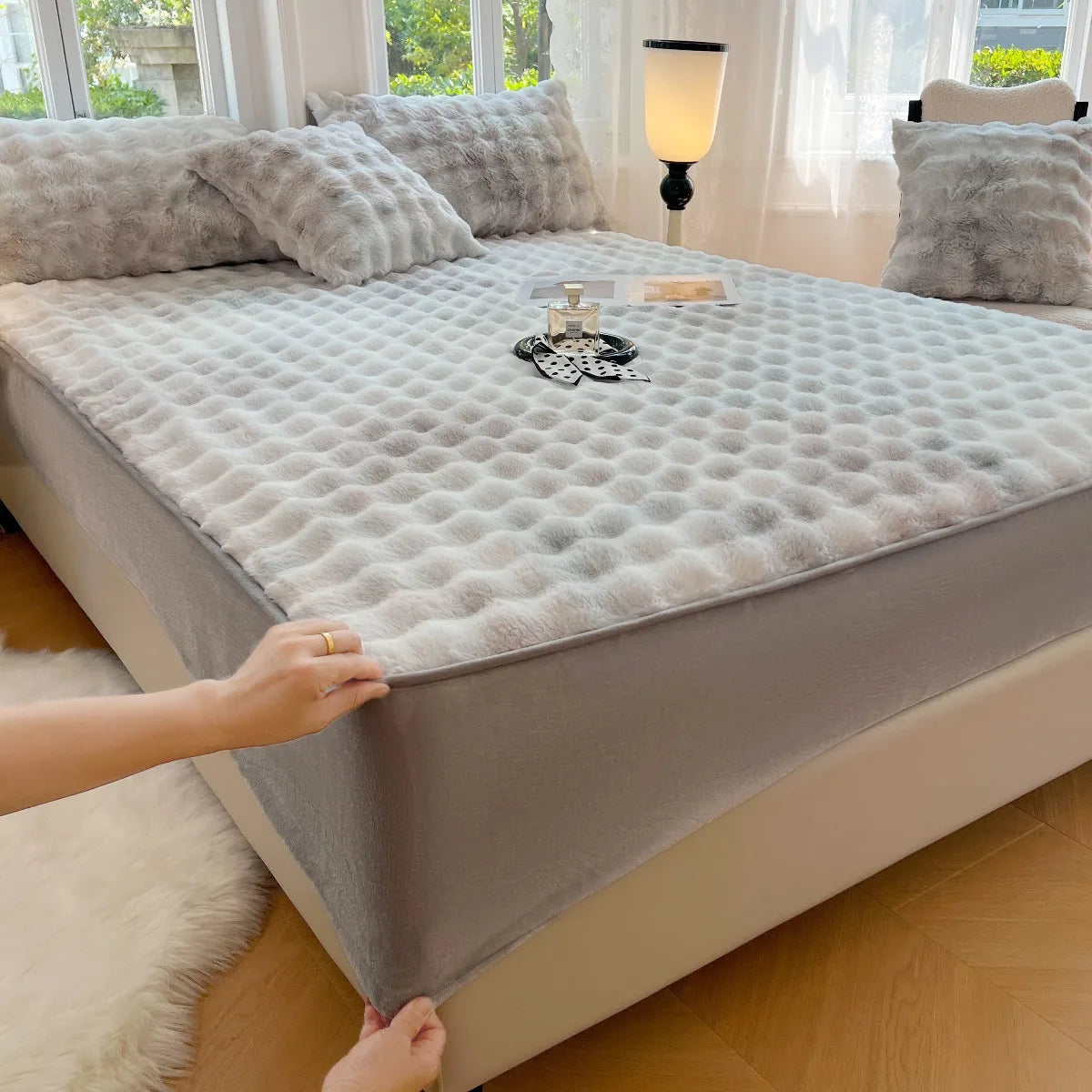 A luxury faux fur fitted sheet and pillowcase set displayed on a bed with white bedding and natural light.