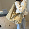 A person is holding a light beige nylon tote bag with a secure zipper closure against a light background.