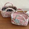 A pink quilted fabric storage basket with a floral pattern is shown on a wooden surface.