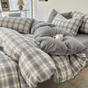 A gray and white plaid bedding set featuring a duvet cover, flat sheet, and pillows on a bed.