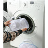 A hand is placing a white mesh laundry bag for bras into the drum of a white washing machine.