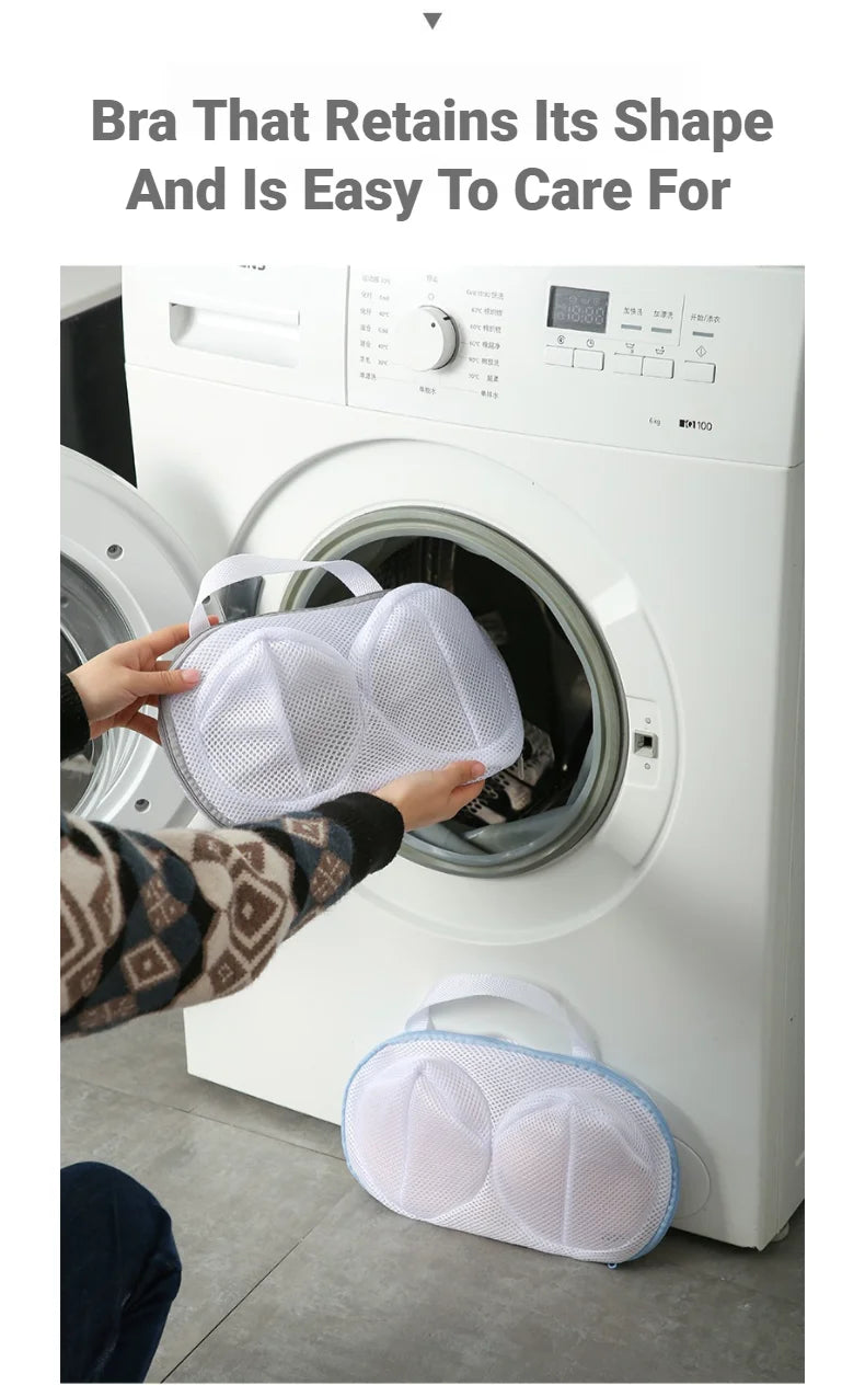 A hand is placing a white mesh laundry bag for bras into the drum of a white washing machine.