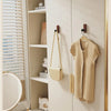 A light beige jacket is hanging on a wooden hook in a modern cabinet with white shelving.
