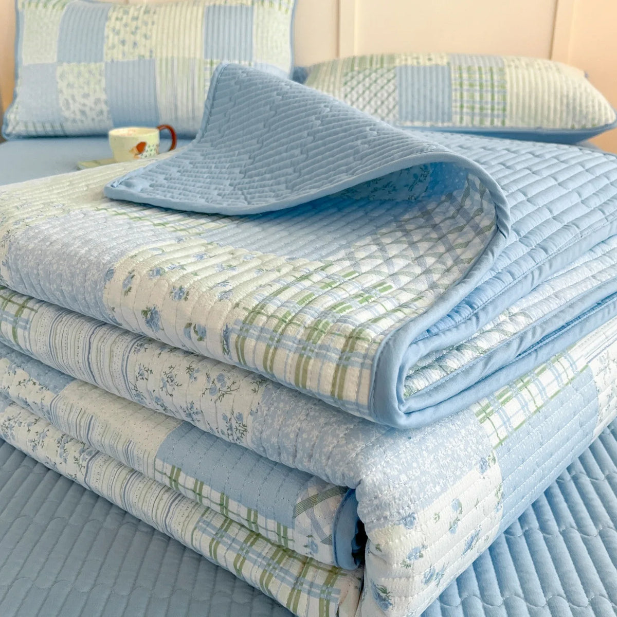 Light blue floral quilted bedspread and pillows stacked on a bed.