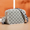 A beige and black patterned compact crossbody bag with a white trim and black strap resting on a light surface.