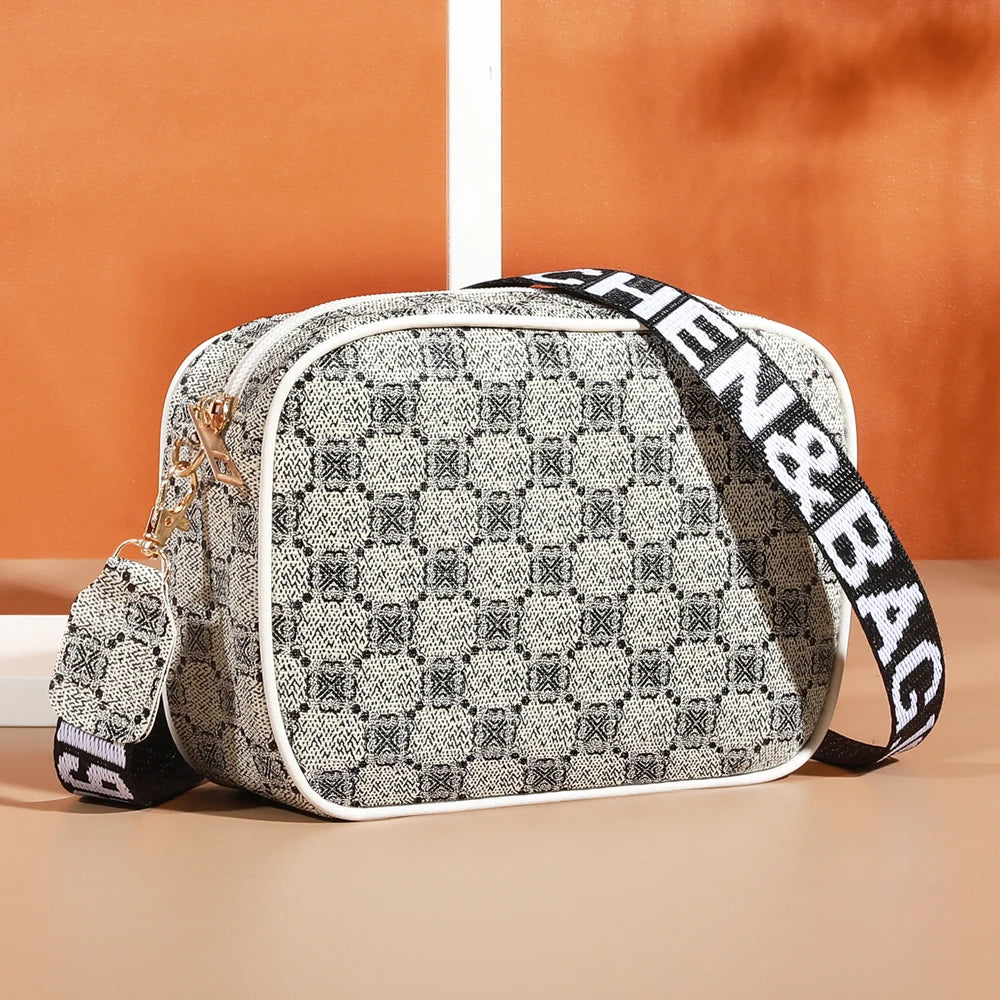 A beige and black patterned compact crossbody bag with a white trim and black strap resting on a light surface.