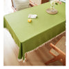 A lime green farmhouse tablecloth with white cotton tassels is displayed on a wooden dining table.