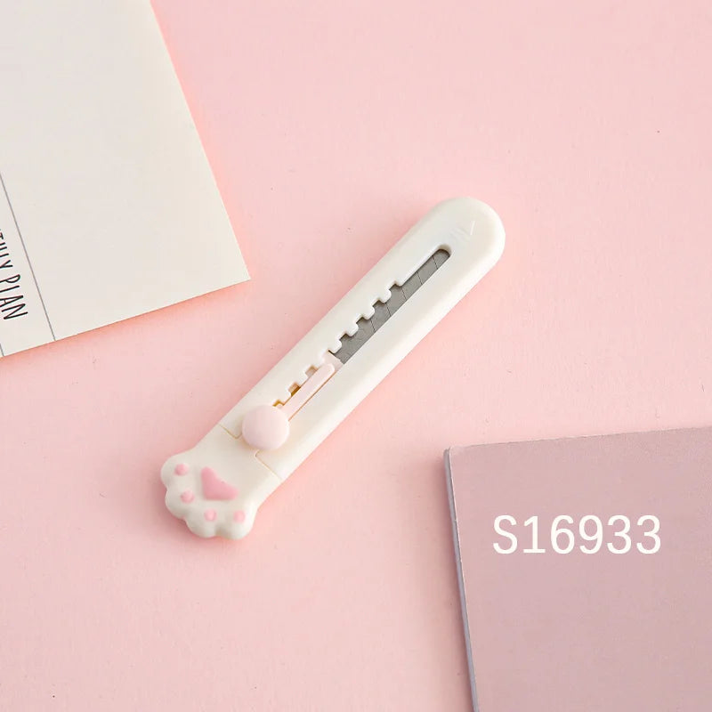 Weiβes Mini-Katzenzange-Messmesser mit rosa Herzdetails auf rosa Hintergrund neben einer Karte.