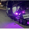 A black motorcycle is parked on a street with purple light reflecting on the pavement.