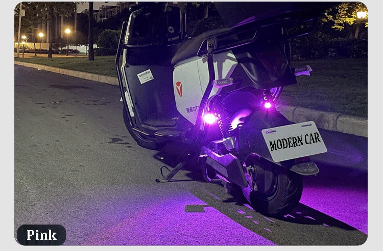 A black motorcycle is parked on a street with purple light reflecting on the pavement.