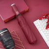 A red automatic foldable umbrella with a silver handle and a black lens is shown on a pink background next to a laptop.