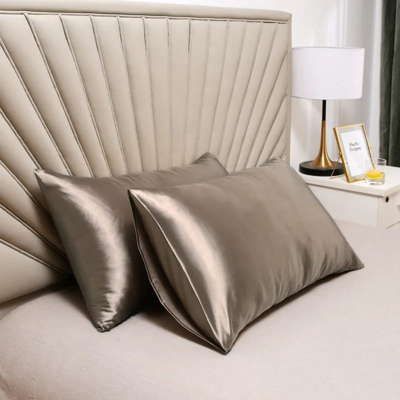 Primer plano de una lujosa funda de almohada de satén en color champán apagado sobre una cama con una lámpara.