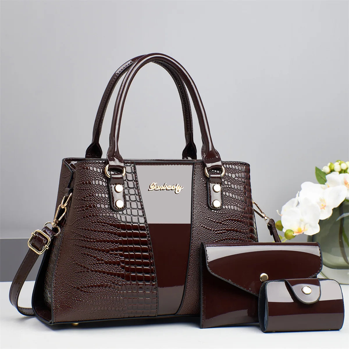 Braunes Krokodilmuster-Patentlederhandtaschen- und Clutch-Set auf weißem Untergrund.