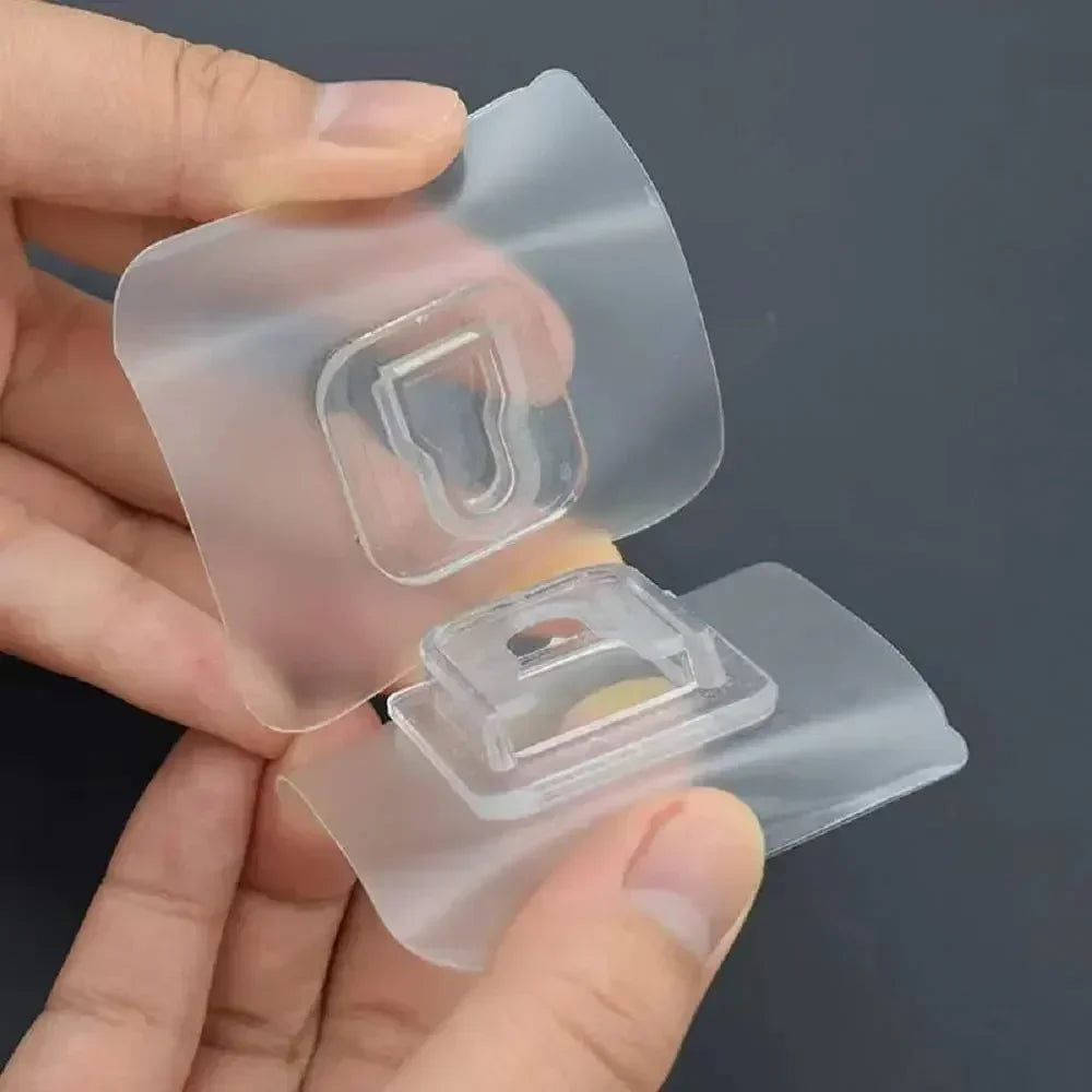 A hand holds clear double-sided adhesive wall hooks, showing the transparent plastic components.