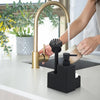 A hand is operating a brass kitchen faucet with a sponge holder and brush accessory on a white countertop.