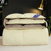 A fluffy white comforter filled with goose and duck down rests on a white surface.