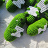 Handcrafted pickle plush with a muppet face made of bright green yarn resting on white fabric.