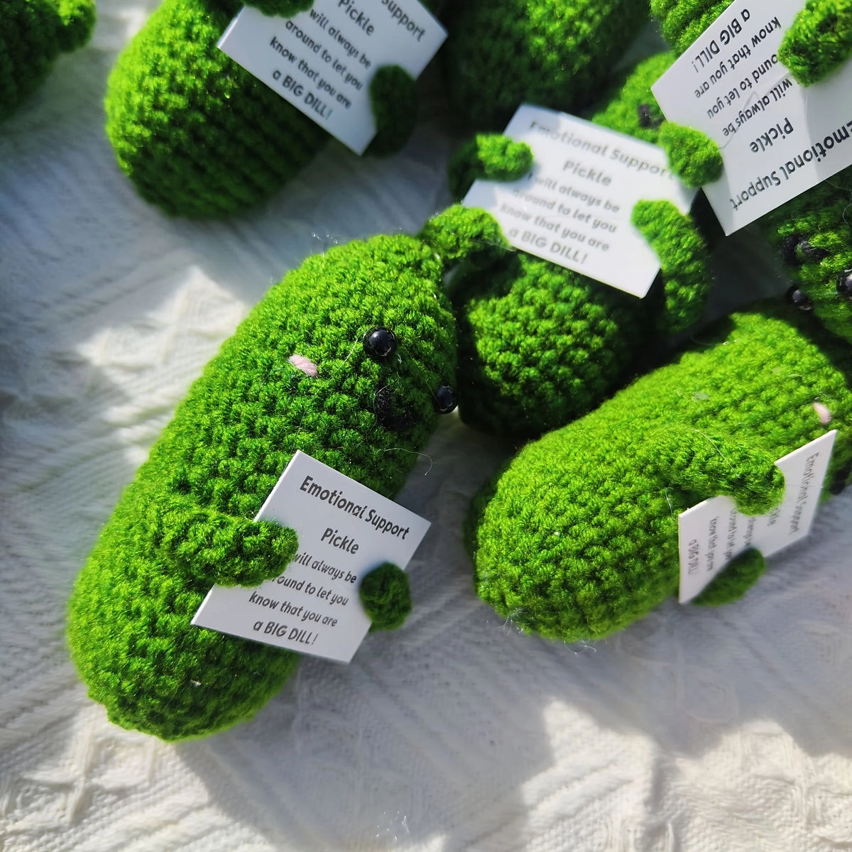 Handcrafted pickle plush with a muppet face made of bright green yarn resting on white fabric.