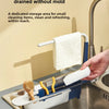 A hand places a white sponge on an adjustable sink holder with a drainer basket in a stainless steel kitchen sink.