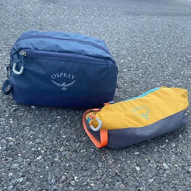 Sac de toilette bleu et pliable à l'eau Osprey posé sur une surface d'asphalte grise.