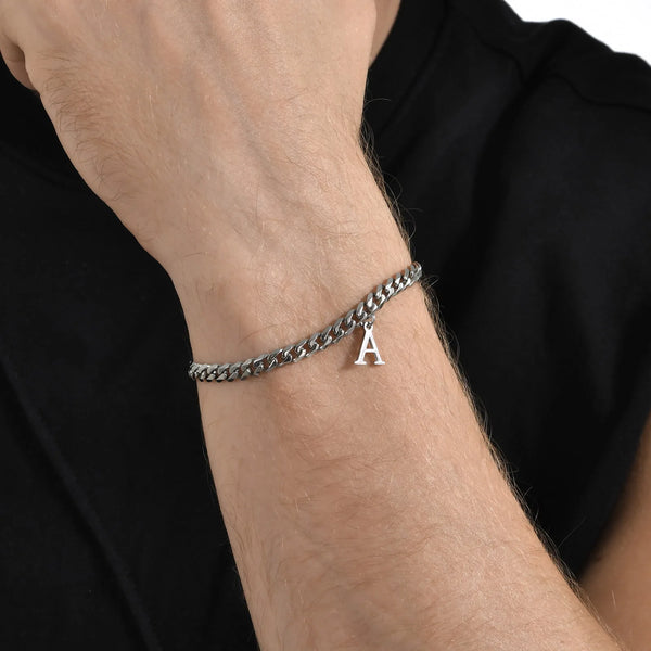 Pulsera de eslabones cubanos plateada con una inicial A, puesta en la muñeca.