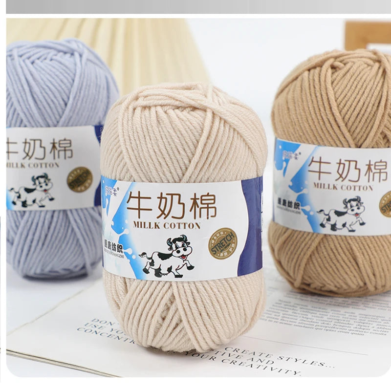 A close-up of a skein of light beige milk cotton blend yarn with a label showing the product name and usage instructions.