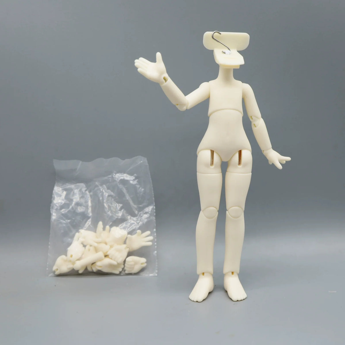 A white articulated BJD collectible figurine standing next to a clear plastic bag containing small white parts.