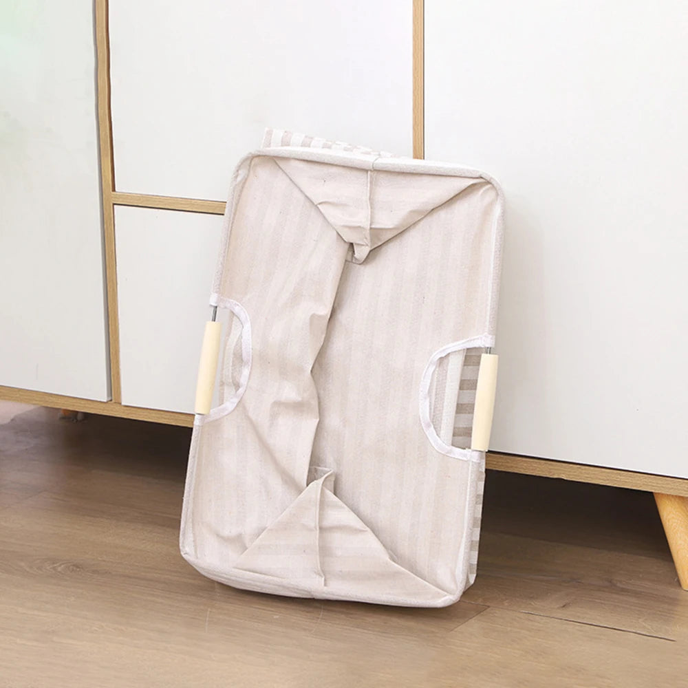 A beige foldable waterproof laundry basket with handles is shown on a wooden floor.