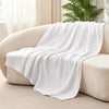A white, textured muslin cotton blanket draped over a light-colored sofa.