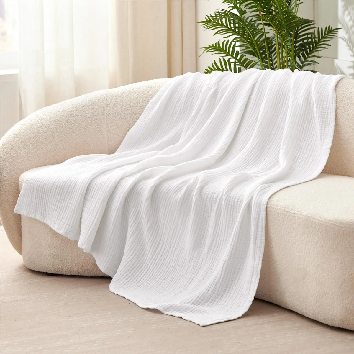 A white, textured muslin cotton blanket draped over a light-colored sofa.