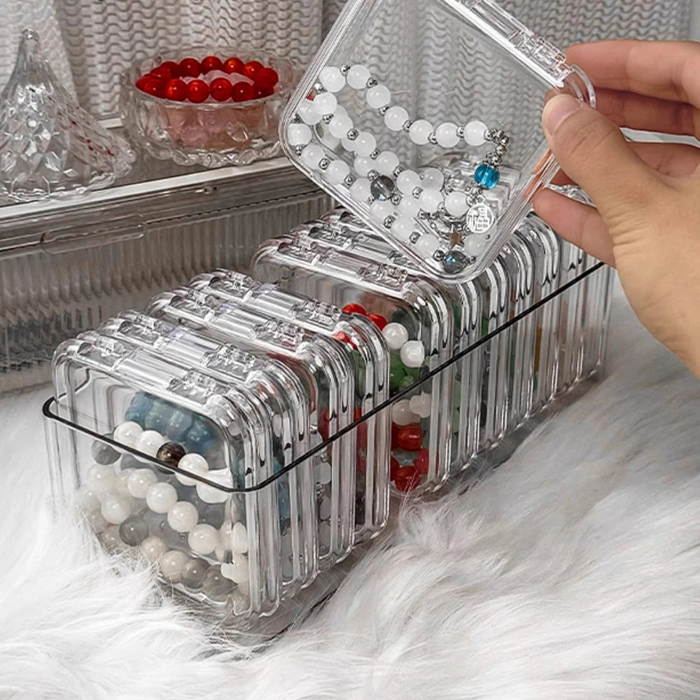 A hand is holding a clear jewelry organizer box with multiple compartments filled with various beads and jewelry.
