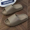 A pair of beige cloud thick-soled EVA slides for men and women resting on a wooden surface.